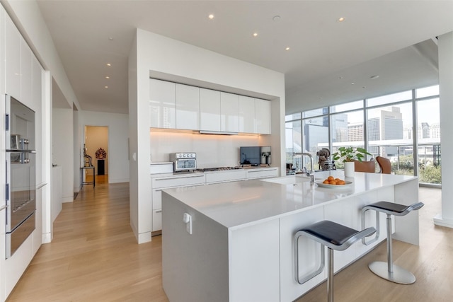 kitchen featuring light wood-type flooring, a center island with sink, white cabinetry, and sink