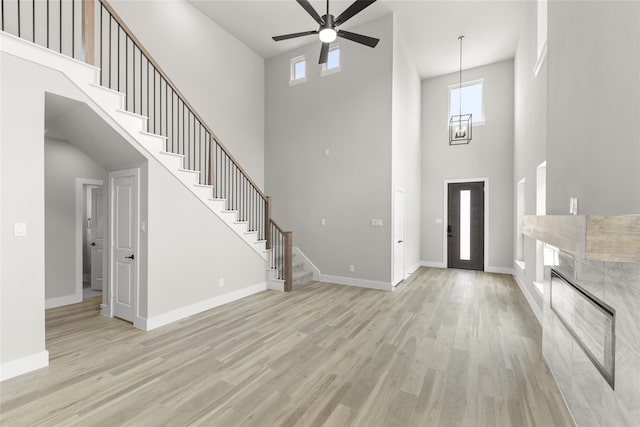 foyer entrance with ceiling fan with notable chandelier, a towering ceiling, and light hardwood / wood-style floors