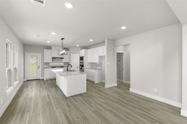 kitchen with light hardwood / wood-style floors, a kitchen island with sink, sink, and white cabinets