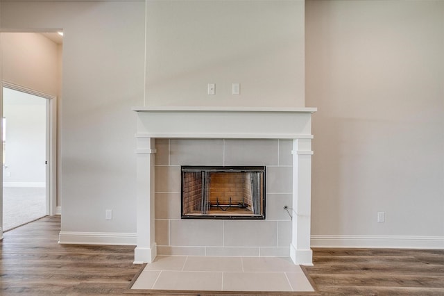 details with baseboards, a tiled fireplace, and wood finished floors