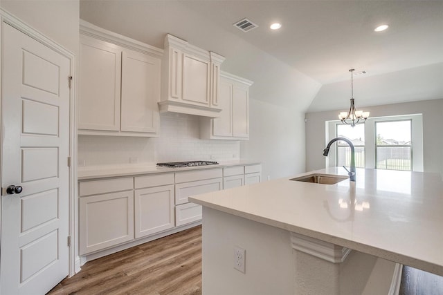 kitchen with a kitchen island with sink, white cabinets, light countertops, and a sink