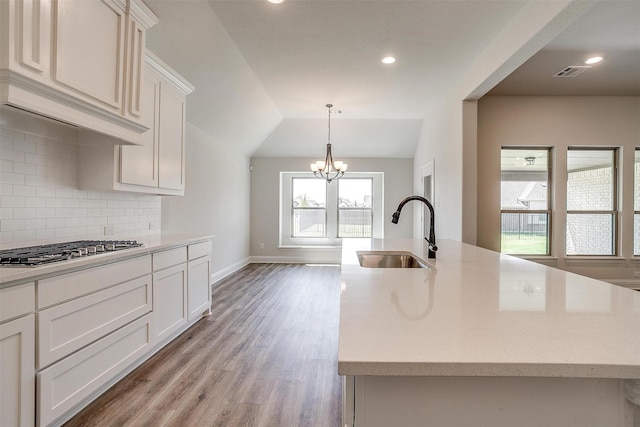 kitchen featuring light countertops, stainless steel gas stovetop, decorative backsplash, a sink, and an island with sink