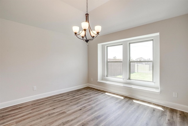 unfurnished room featuring light wood-type flooring, an inviting chandelier, and baseboards