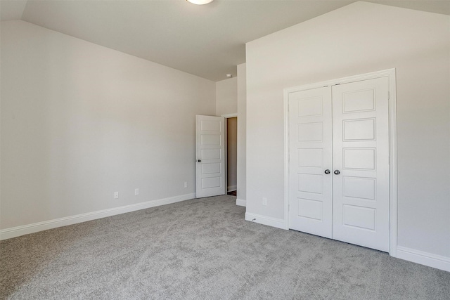 unfurnished bedroom with lofted ceiling, light carpet, baseboards, and a closet