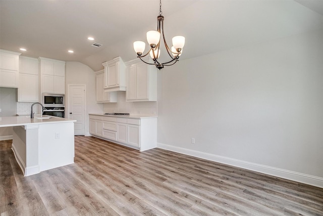 kitchen with white cabinetry, an island with sink, stainless steel oven, built in microwave, and hanging light fixtures