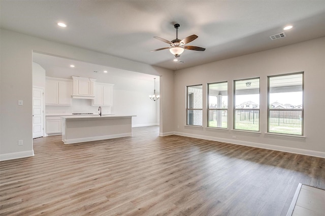 unfurnished living room featuring ceiling fan with notable chandelier, sink, and light wood-type flooring