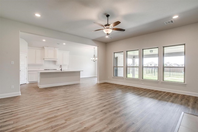 unfurnished living room with recessed lighting, ceiling fan with notable chandelier, visible vents, baseboards, and light wood finished floors