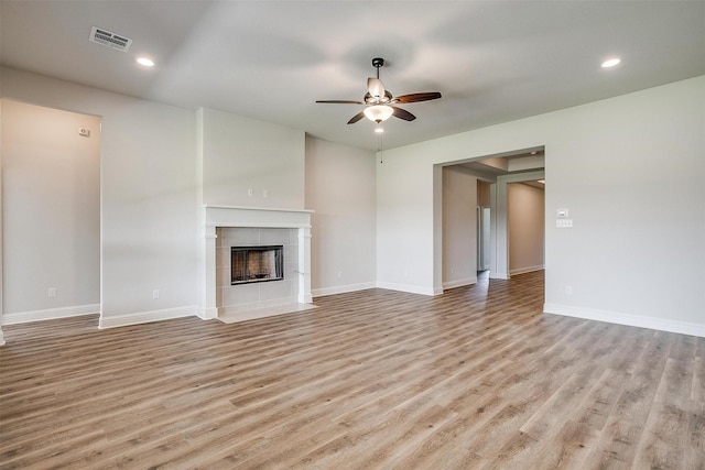 unfurnished living room with a tile fireplace, ceiling fan, light wood-style flooring, and baseboards