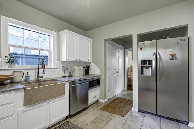 kitchen featuring appliances with stainless steel finishes, backsplash, sink, dark stone countertops, and white cabinetry