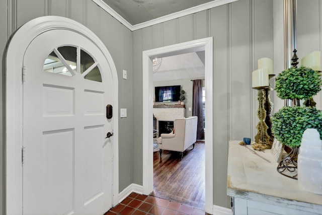 entrance foyer with dark tile patterned flooring, ornamental molding, and a brick fireplace