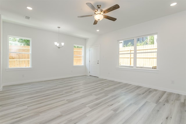 unfurnished room featuring ceiling fan with notable chandelier, light wood-type flooring, and plenty of natural light