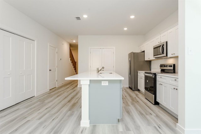 kitchen with white cabinets, appliances with stainless steel finishes, a center island with sink, and light hardwood / wood-style flooring