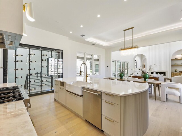 kitchen with appliances with stainless steel finishes, hanging light fixtures, light hardwood / wood-style floors, a center island with sink, and sink