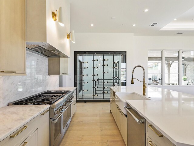 kitchen with backsplash, stainless steel appliances, light hardwood / wood-style flooring, sink, and wall chimney range hood