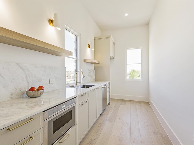 kitchen featuring appliances with stainless steel finishes, light hardwood / wood-style floors, sink, and light stone counters