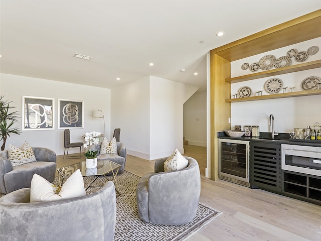 living room featuring light wood-type flooring, wet bar, and beverage cooler