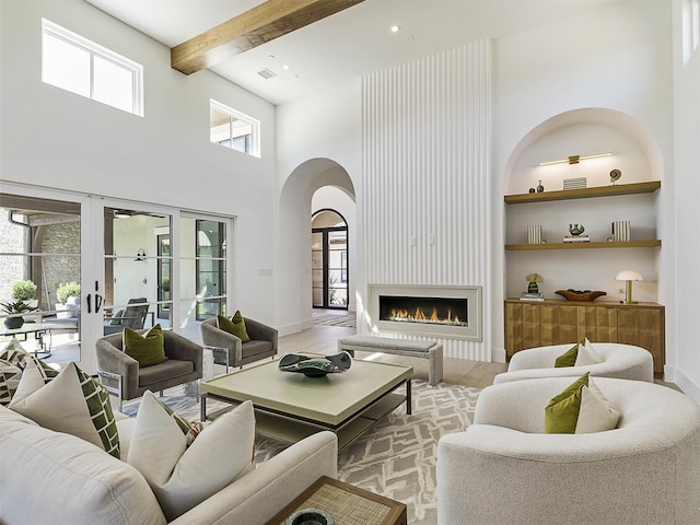 living room featuring beamed ceiling, built in shelves, a fireplace, light hardwood / wood-style flooring, and a high ceiling