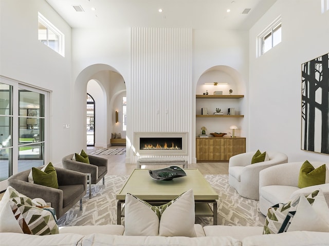 living room featuring light wood-type flooring, a high ceiling, a fireplace, and built in features