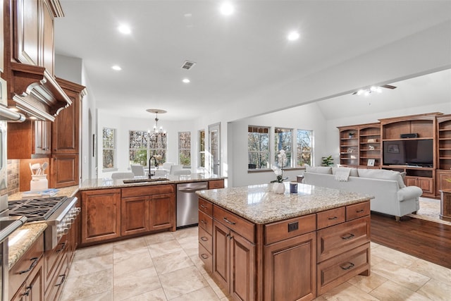 kitchen with sink, appliances with stainless steel finishes, light stone counters, a kitchen island, and decorative light fixtures