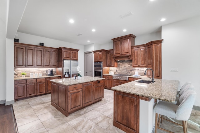 kitchen featuring light stone countertops, appliances with stainless steel finishes, tasteful backsplash, sink, and a center island with sink