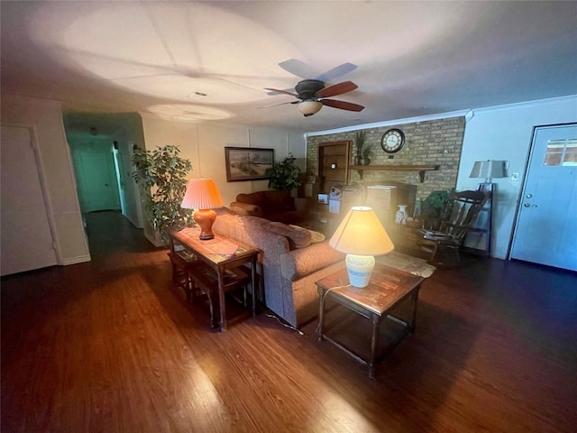 living room with a brick fireplace, ornamental molding, ceiling fan, and dark wood-type flooring