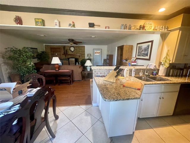 kitchen with ceiling fan, sink, a brick fireplace, light tile floors, and light stone counters