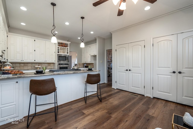 kitchen featuring light stone countertops, a kitchen bar, stainless steel appliances, pendant lighting, and white cabinetry