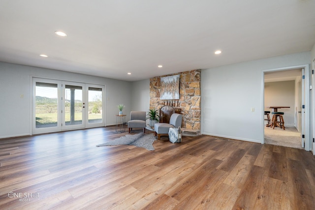 sitting room with a stone fireplace, light hardwood / wood-style flooring, and french doors