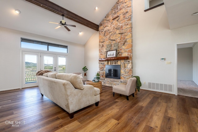 living room with ceiling fan, a stone fireplace, beamed ceiling, a towering ceiling, and hardwood / wood-style flooring