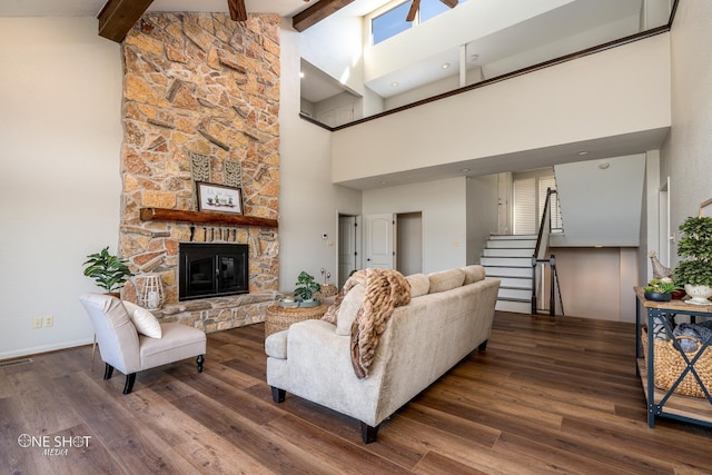 living room featuring beam ceiling, a towering ceiling, dark hardwood / wood-style floors, and a stone fireplace