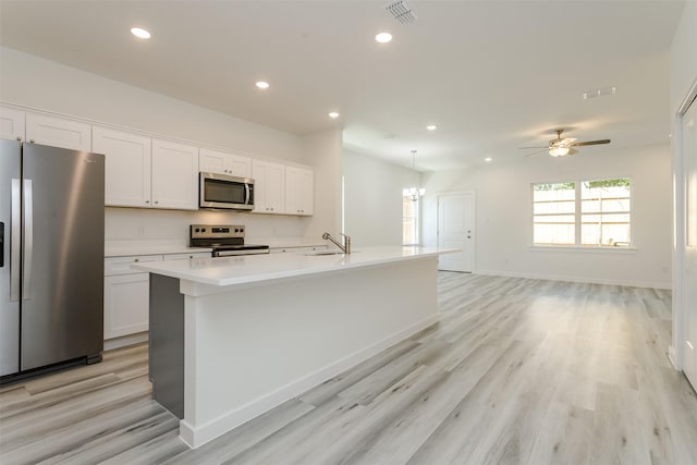 kitchen featuring white cabinets, ceiling fan with notable chandelier, stainless steel appliances, and an island with sink