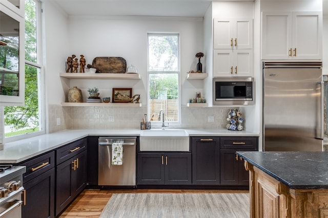 kitchen with built in appliances, light hardwood / wood-style floors, tasteful backsplash, white cabinets, and sink