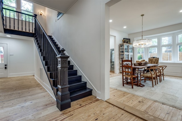 staircase with a chandelier, plenty of natural light, and light wood-type flooring