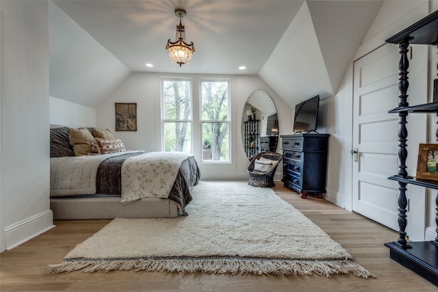 bedroom with lofted ceiling, an inviting chandelier, and light wood-type flooring