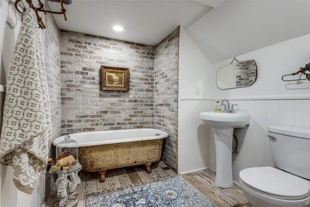 bathroom featuring brick wall, hardwood / wood-style floors, toilet, and a tub