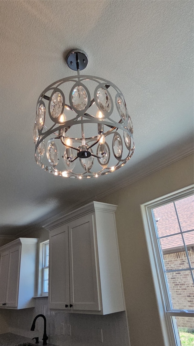 room details featuring ornamental molding, white cabinetry, an inviting chandelier, and a textured ceiling