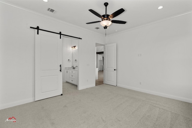 unfurnished bedroom with ceiling fan, connected bathroom, light carpet, and a barn door