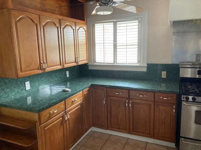 kitchen featuring gas stove, backsplash, ceiling fan, and light tile floors