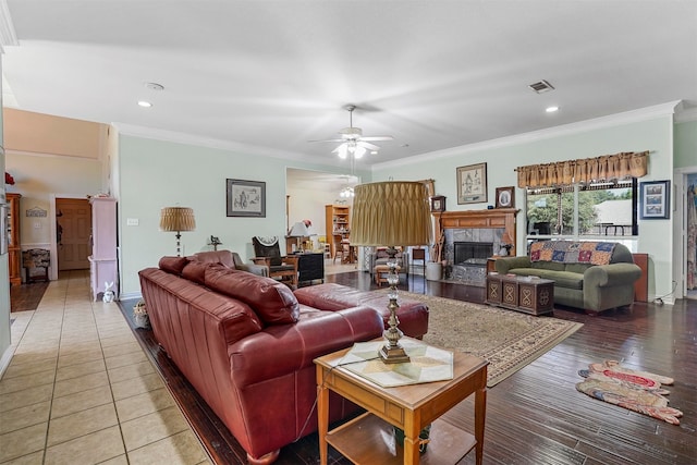 living room featuring a tiled fireplace, crown molding, ceiling fan, and wood-type flooring