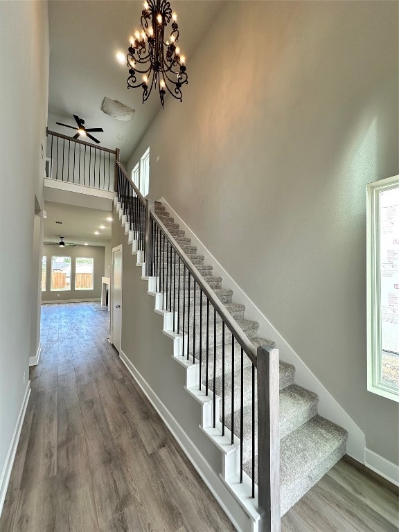 stairway featuring ceiling fan with notable chandelier, a towering ceiling, and hardwood / wood-style floors