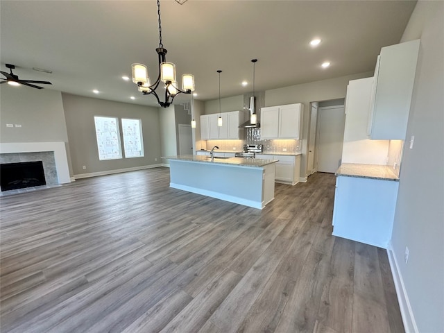 kitchen with pendant lighting, wall chimney range hood, white cabinets, light wood-type flooring, and sink