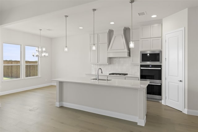 kitchen featuring stainless steel appliances, premium range hood, hardwood / wood-style flooring, decorative light fixtures, and sink