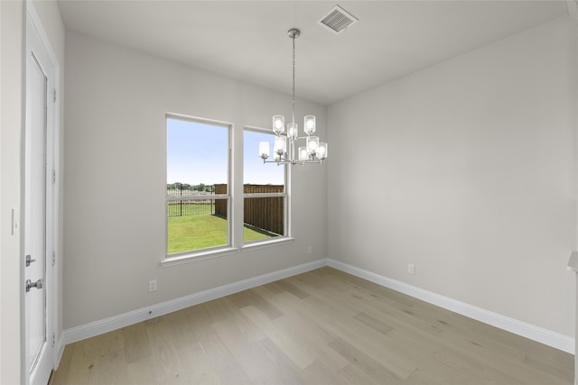 empty room featuring a notable chandelier and light hardwood / wood-style flooring