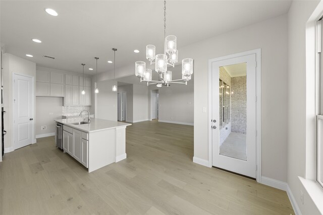 kitchen featuring an island with sink, sink, pendant lighting, and light hardwood / wood-style flooring