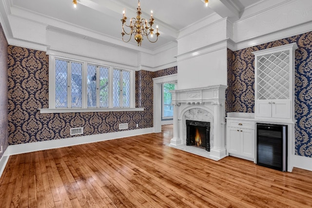 unfurnished living room featuring a high end fireplace, beamed ceiling, light hardwood / wood-style floors, beverage cooler, and a notable chandelier