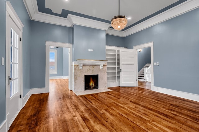 unfurnished living room featuring a raised ceiling, a premium fireplace, dark hardwood / wood-style flooring, a chandelier, and ornamental molding