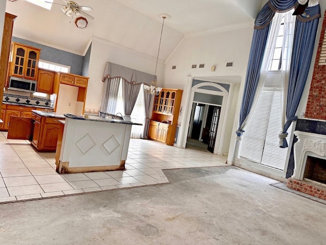 kitchen with ceiling fan, high vaulted ceiling, a brick fireplace, dark stone countertops, and crown molding