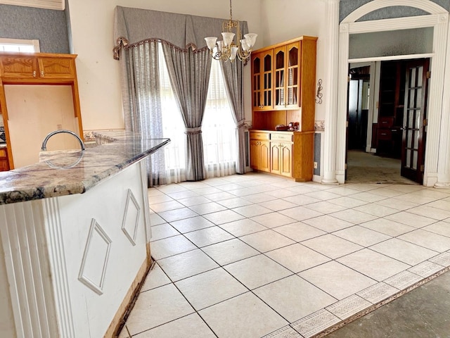 kitchen featuring kitchen peninsula, pendant lighting, light stone counters, a chandelier, and light tile flooring