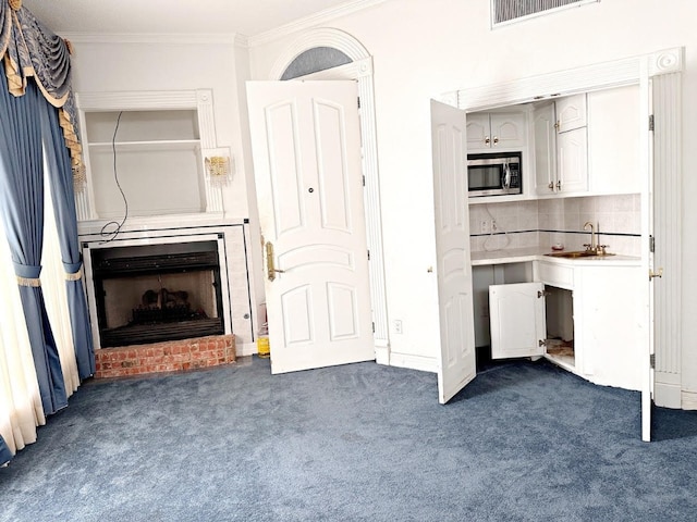 kitchen featuring a brick fireplace, sink, backsplash, stainless steel microwave, and ornamental molding