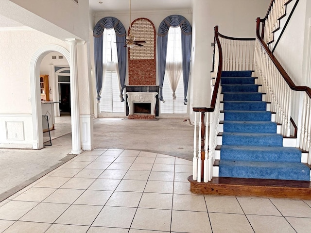 staircase featuring light tile floors, a fireplace, ceiling fan, crown molding, and decorative columns